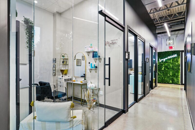 A picture of a salon suite with glass walls, a black chair, and a gold makeup table.