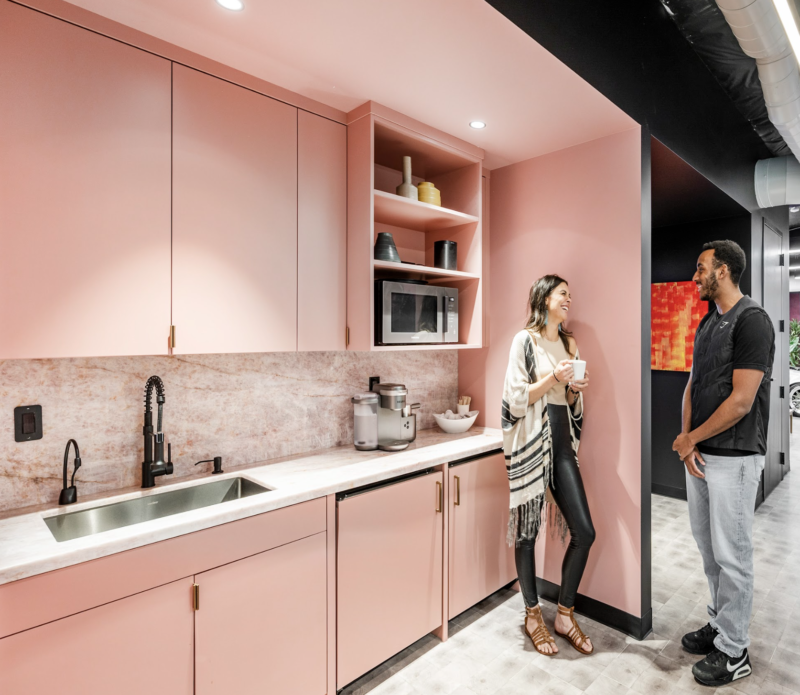 A stylish pink kitchenette with two colleagues chatting.